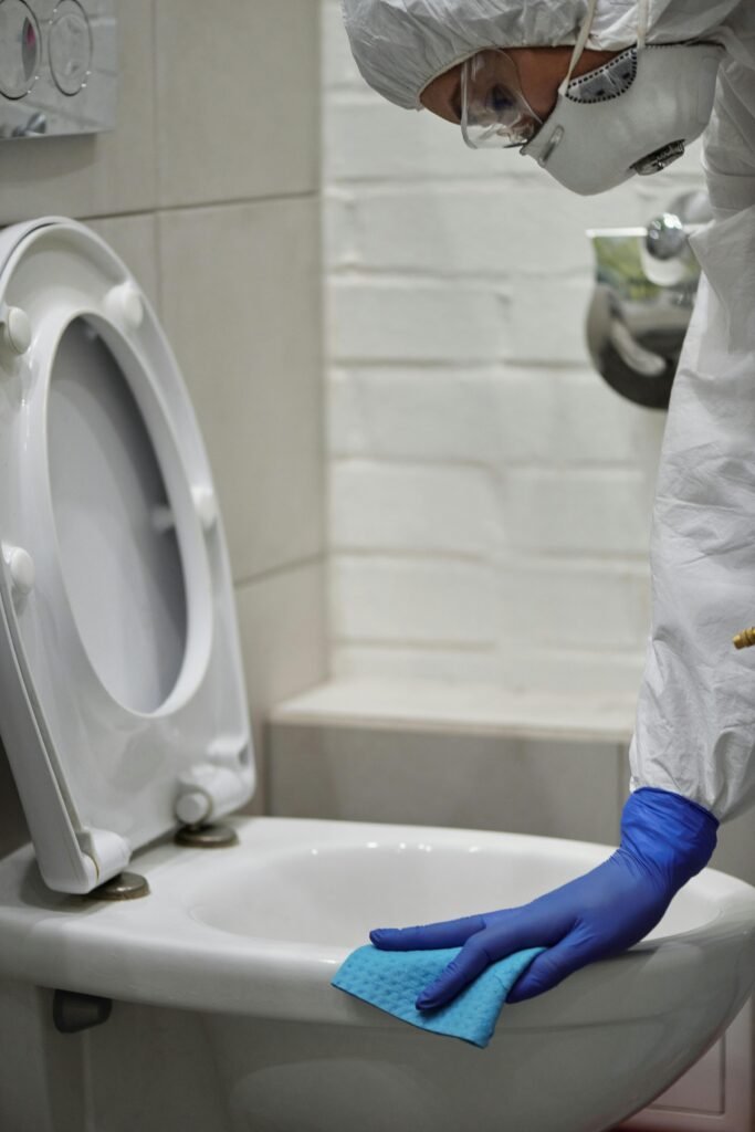 Person in protective gear cleaning a toilet for sanitation and safety.
