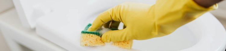 From above of crop anonymous person in rubber gloves using soapy sponge while cleaning toilet bowl